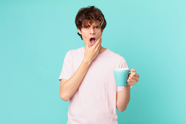 young man with a coffee mug with mouth and eyes wide open and hand on chin - Foto, Imagem