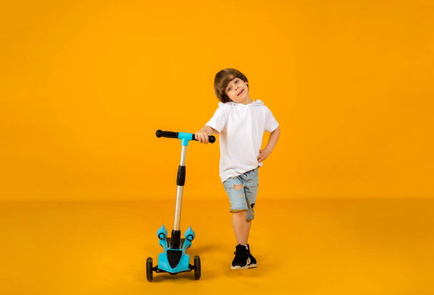 small boy stands with a scooter on a yellow background with space for text. Sports for children - Foto, Bild