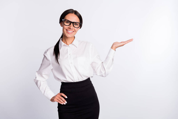 Photo of optimistic brunette hairdo lady hold empty space wear spectacles white shirt isolated on grey color background - Foto, immagini