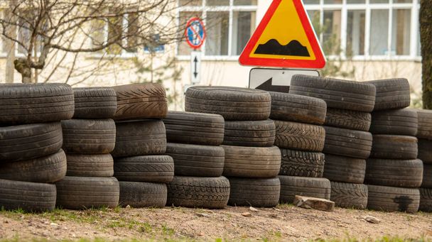 сложенные старые шины легковых автомобилей лежат на земле рядом с дорогой, фон - Фото, изображение