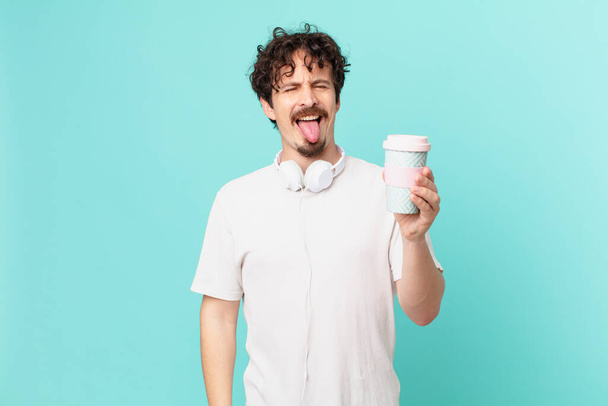 mladý muž s kávou s veselým a vzpurným postojem, vtipem a vystrčeným jazykem - Fotografie, Obrázek