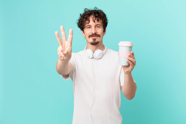 young man with a coffee smiling and looking friendly, showing number three - Photo, image