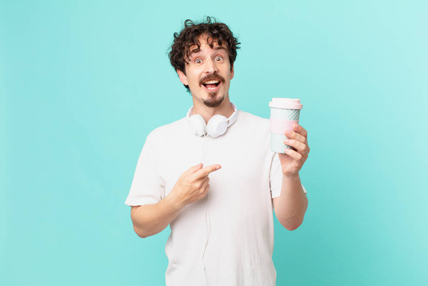 young man with a coffee looking excited and surprised pointing to the side - Foto, Imagem