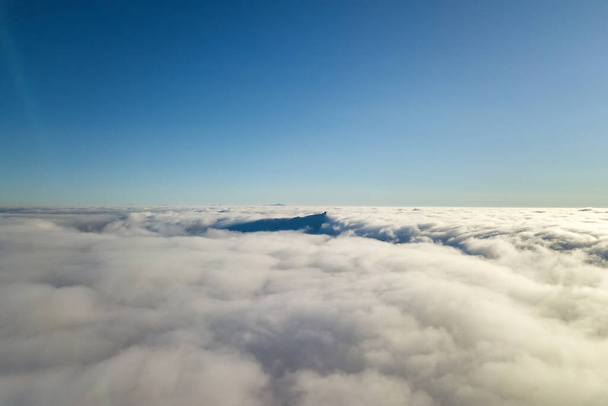 Widok z lotu ptaka nad białymi chmurami i odległym szczytem góry w słoneczny dzień. - Zdjęcie, obraz