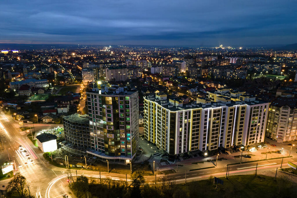 Wysokie budynki mieszkalne z oświetlonymi oknami w dzielnicy mieszkalnej miasta w nocy. - Zdjęcie, obraz