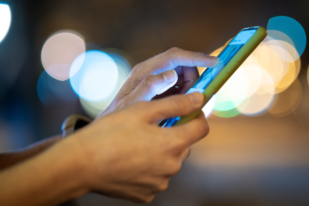 Detailní záběr ženských rukou držících mobilní telefon procházení internetu na ulici města s rozmazanými světly v noci. - Fotografie, Obrázek