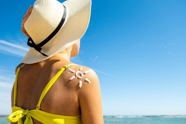 Back view of young woman tanning at the beach with sunscreen cream in sun shape on her shoulder. UV sunburn protection and sunblock skincare concept - Photo, Image