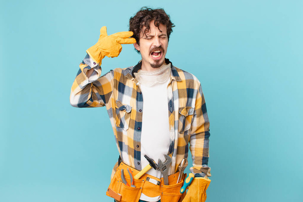young handyman housekeeper looking unhappy and stressed, suicide gesture making gun sign - Foto, imagen