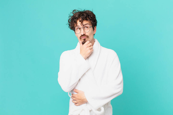 young man wearing bathrobe thinking, feeling doubtful and confused - Foto, Imagem