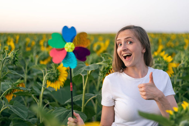 Fröhliches Mädchen mit Windmühlenspielzeug auf Sonnenblumenfeld im Hintergrund. Grünes Energiekonzept. - Foto, Bild