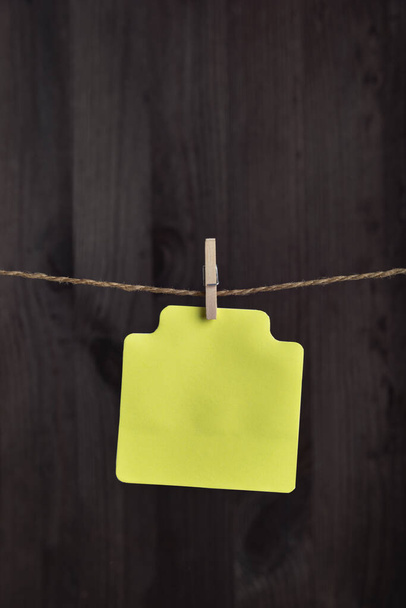 Blank yellow paper card hang with clothespin on rope. Copy space. Place for your text. Vertical frame. - Photo, Image