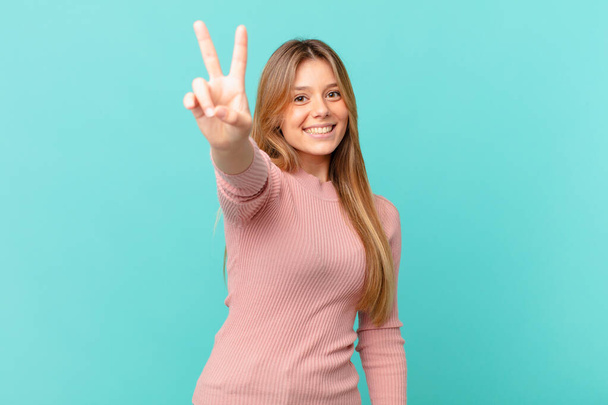 young pretty woman smiling and looking happy, gesturing victory or peace - Фото, зображення