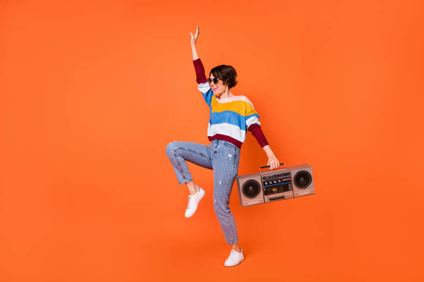 Full length portrait of cheerful cool girl arm holding recorder enjoy dance isolated on orange color background - Foto, Bild