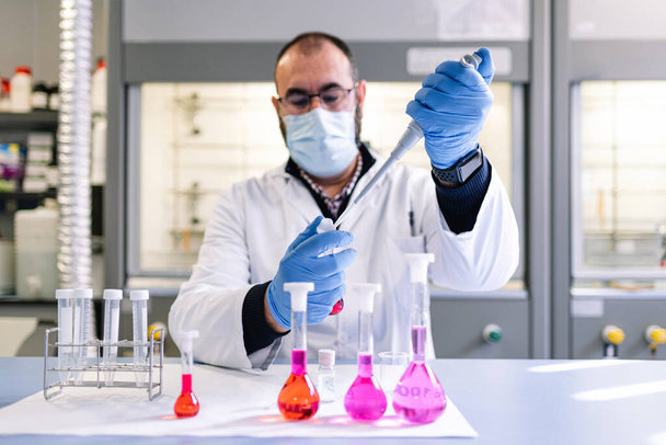 Laboratuvar teknisyeni kırmızı sıvıyla pipetini bir kimya laboratuvarında analiz için tutuyor..  - Fotoğraf, Görsel