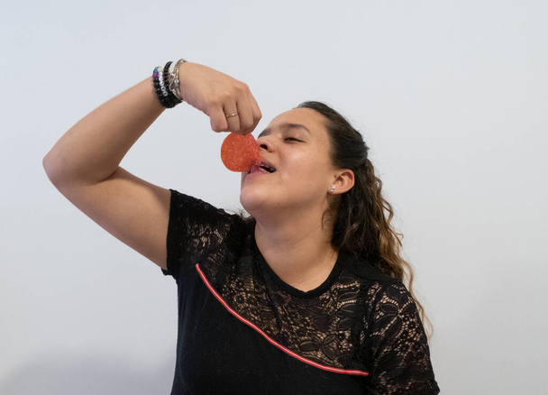 jonge vrouw eet slice van salami op witte achtergrond - Foto, afbeelding
