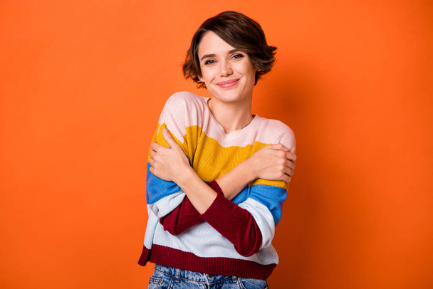 Portrait of attractive cheerful girl hugging herself enjoying soft clothes isolated over bright orange color background - Fotoğraf, Görsel