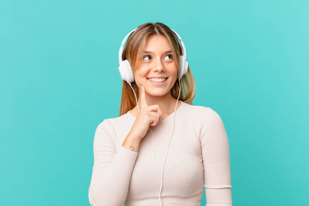 young woman with headphones smiling happily and daydreaming or doubting - Photo, image