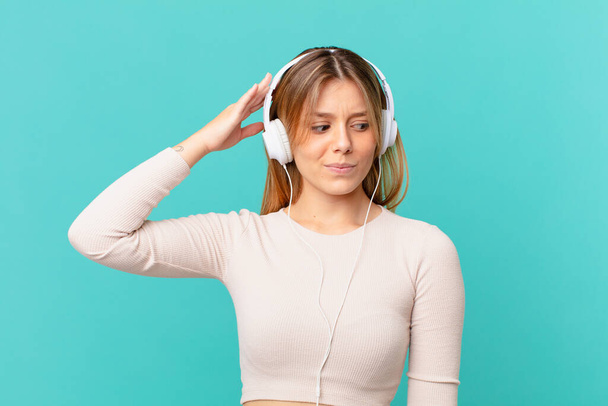 young woman with headphones feeling puzzled and confused, scratching head - Photo, Image