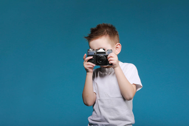 Mały chłopiec robi zdjęcie kamerą retro. Chłopiec z klasycznym aparatem fotograficznym na niebieskim tle. Stara technologia z przestrzenią do kopiowania. Fotografia edukacyjna dziecka . - Zdjęcie, obraz