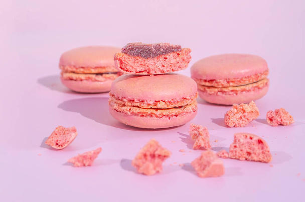 Tasty pink raspberry macarons on light violet background. French homemade dessert with small broken pieces. High quality photo - Fotoğraf, Görsel