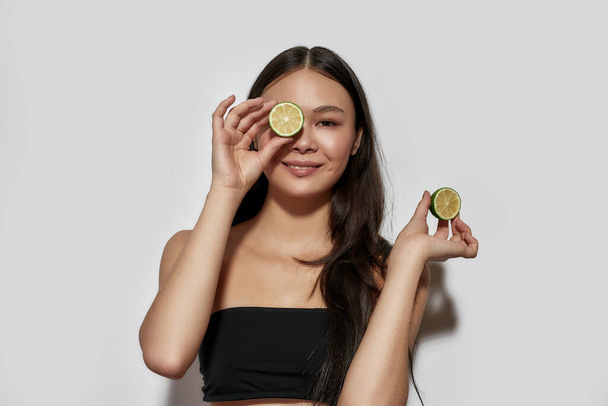 alegre joven asiático chica holding limón rebanada cerca ojo - Foto, Imagen