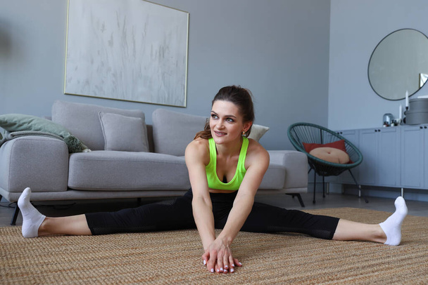 Jonge vrouw doet stretching oefeningen thuis - Foto, afbeelding