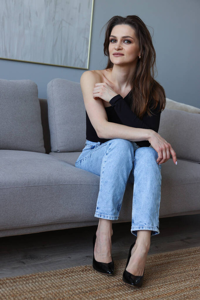 Fashion portrait of a young woman in a black T-shirt and jeans at home - Photo, Image