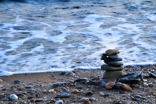 Piedras redondas apiladas en la playa Isla Plana al atardecer en Cartagena. Ondas en el fondo. - Foto, Imagen