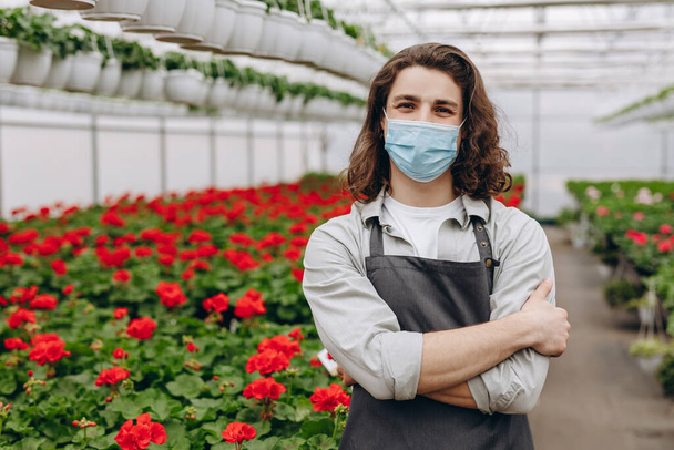 Männlicher Florist mit Maske, während er im Blumenladen arbeitet. Gartencenter und Einkaufskonzept in Quarantäne - Foto, Bild