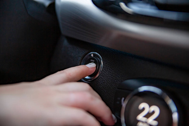 el dedo de la mano del conductor presiona el botón de parada de arranque en un coche moderno. Primer plano. sin cara. opción sin llave en el coche. enfoque selectivo - Foto, imagen
