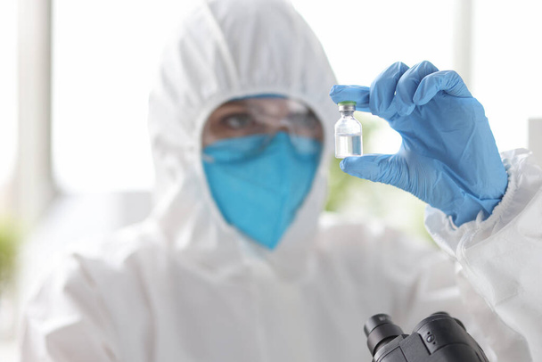 Researcher in protective suit looks at medicine bottle. - Photo, Image