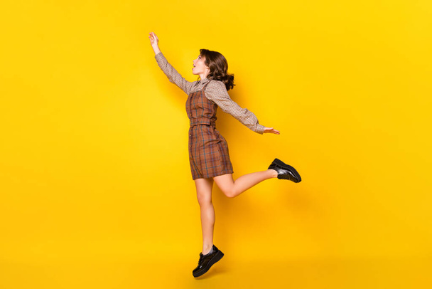 Full size profile photo of optimistic funny brunette lady jump arm wear shirt dress sneakers isolated on vivid yellow background - Photo, image
