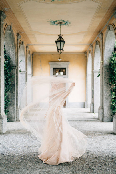 La novia en un vestido de novia se cubre con un velo en una antigua terraza con columnas. Lago de Como - Foto, imagen