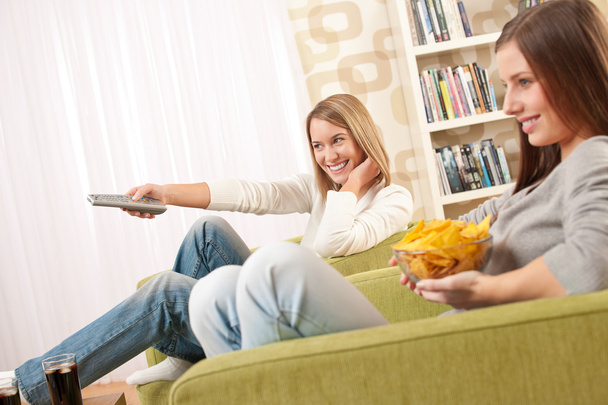 Студенти - Дві жінки-підліток дивиться телевізор і їсть чіпси в сучасному лаунжі
 - Фото, зображення