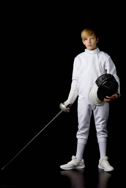 Boy in fencing costume holding mask and sabre - 写真・画像