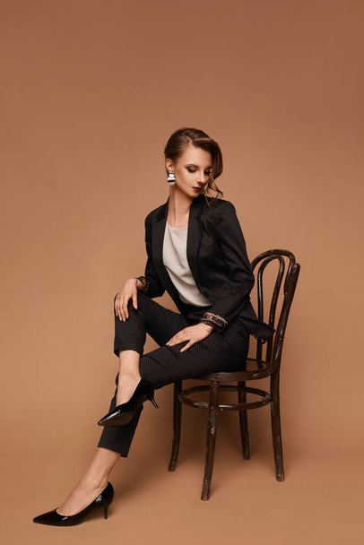 Young caucasian model woman in a grey suit, blouse and black shoes sitting on the chair on beige background, isolated with copy space - Foto, Imagem