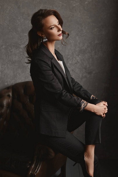 Stylish young woman, an office worker in a stylish suit and white blouse posing on the vintage armchair - Photo, image