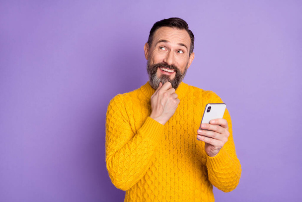 Photo of minded man hold telephone finger chin look up empty space wear yellow sweater isolated violet background - Foto, Imagem