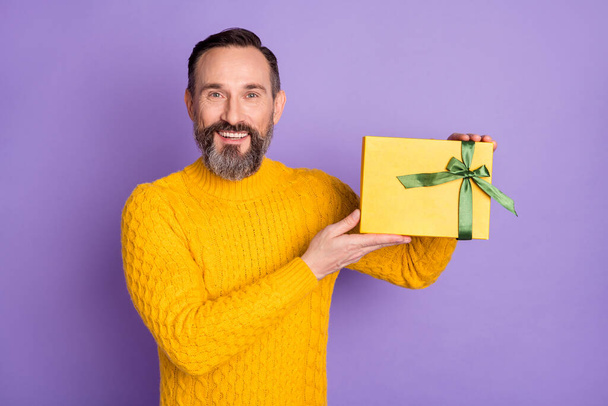 Photo of positive man hold giftbox toothy beaming smile wear yellow pullover isolated violet background - Фото, изображение