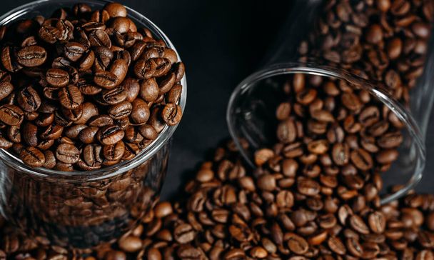 Glass transparent cup full of brown coffee beans, many coffee beans on a black background. Close-up. View from above. - Valokuva, kuva