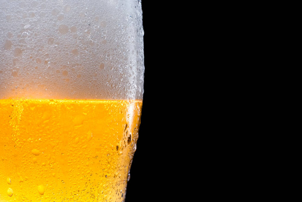 Half beer glass with beer and foam on a black background. Space for text and logo. - Photo, image