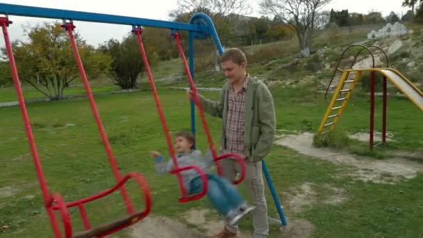 Ojciec kołysząc syna małe na plac zabaw dla dzieci - Materiał filmowy, wideo