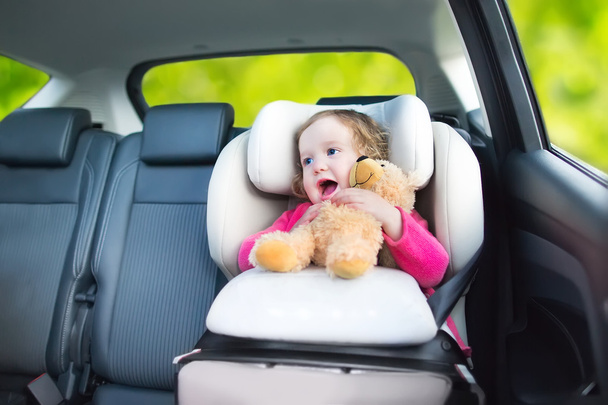 Милая кудрявая девочка с игрушечным медвежонком наслаждается поездкой на машине
 - Фото, изображение