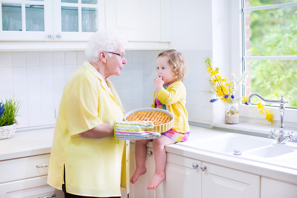 ευτυχισμένη γιαγιά και κοριτσάκι ψήσιμο μια πίτα σε ένα λευκό σαλοκουζίνα - Φωτογραφία, εικόνα