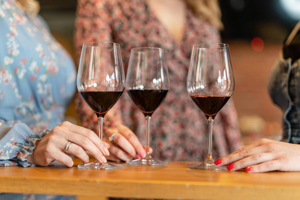 Κοντινό πλάνο στα χέρια άγνωστων γυναικών που κρατούν ένα ποτήρι κόκκινο κρασί στο τραπέζι - Φωτογραφία, εικόνα