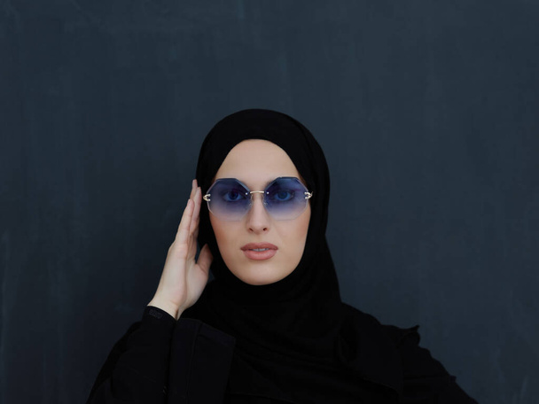 Fiatal muszlim a hagyományos ruhák vagy abaya és napszemüveg pózol előtt fekete tábla. Arab nő képviseli a modern arab életmód, iszlám divat és Ramadan Kareem koncepció - Fotó, kép