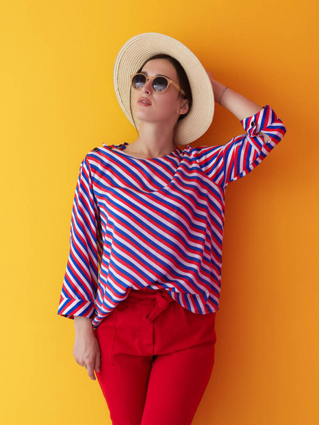 Portrait of young woman wearing sunglasses and hat over a yellow background. Female model posing in the studio. Concept of fashion - Фото, зображення
