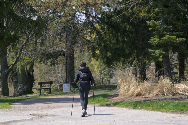 Ενεργός ηλικιωμένη γυναίκα που περπατά στο πάρκο με τους πόλους πεζοπορίας - Φωτογραφία, εικόνα