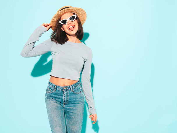 Portrait of young beautiful smiling female in trendy summer hipster  clothes. Sexy carefree woman posing near blue wall in studio. Positive model having fun in sunglasses and hat. Cheerful and happy - Foto, immagini