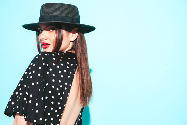 High fashion portrait of young beautiful brunette woman wearing nice trendy summer polka-dot dress .Sexy fashion model posing near blue wall in studio.Fashionable female with red lips and hat - Fotografie, Obrázek